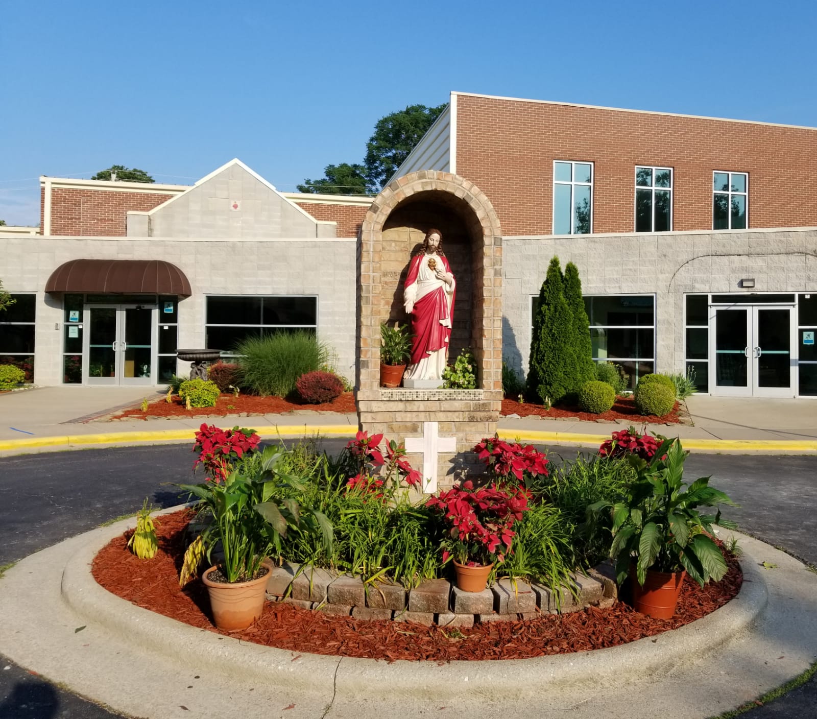 Exterior of the church with a statue of The Lord Jesus Christ with his Sacred Heart and flowers